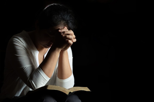 a woman praying in the dark with a bible